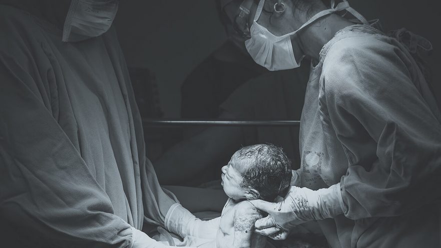 Black and white photo of baby being delivered by two doctors